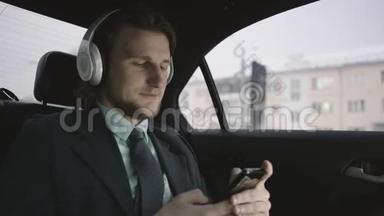 一个英俊的男人，棕色头发，穿着开心果衬衫，穿着灰色西装，坐在车里，通过手机输入信息，听着